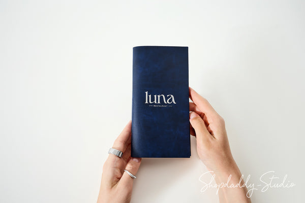 A person's hands holding a small navy blue notebook with the brand name 'luna' printed in white on the front, set against a plain white background.