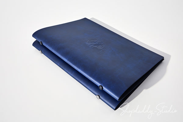 A dark blue leather folio or binder with a stitched cover and metal snap fasteners, shown on a clean white background with a soft shadow. A 'ShopDaddy-Studio' watermark is visible in the bottom right corner.