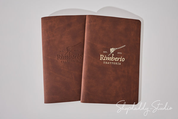 Two brown leather-bound booklets or menus with the 'Rimberio Trattoria' logo, displayed against a light gray background.