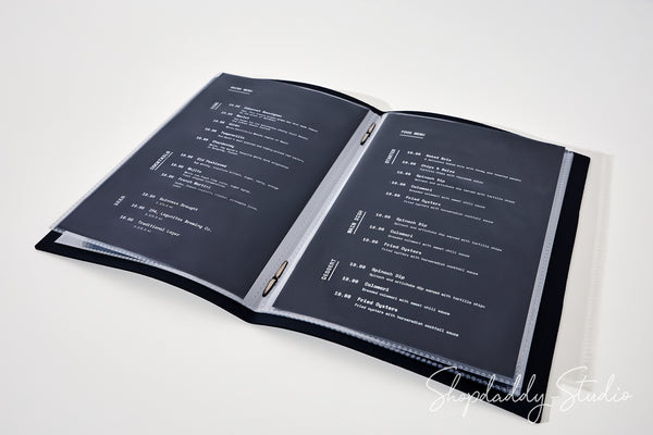 An open black binder or menu folder with two dark gray pages printed with white text, photographed on a clean white background. A faint 'Shopaddy Studio' watermark appears in the lower right corner.