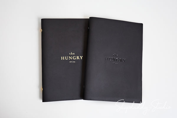 Two black hardcover books or portfolios titled 'the HUNGRY' with gold lettering, displayed side by side on a plain white background.