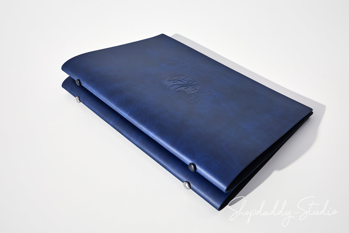 A dark blue leather folio or binder with a stitched cover and metal snap fasteners, shown on a clean white background with a soft shadow. A 'ShopDaddy-Studio' watermark is visible in the bottom right corner.