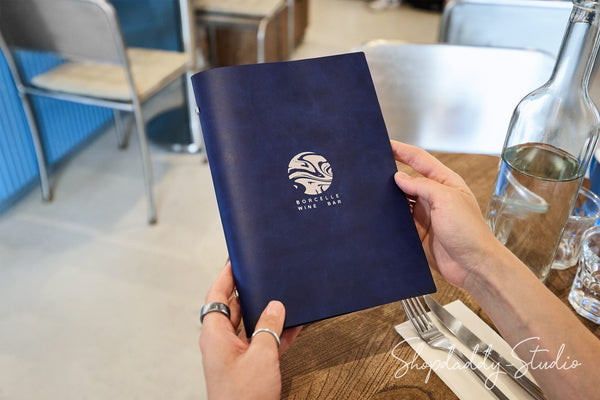 A navy blue menu or book held by two hands in a restaurant setting, featuring a white circular logo and the text 'MURPHY'S MINE BAR'.