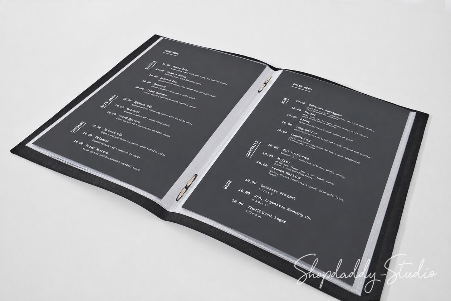 An open black binder or menu folder with two dark gray pages printed with white text, photographed on a light gray background. A script watermark reading Shopdaddy-Studio appears in the lower right corner.