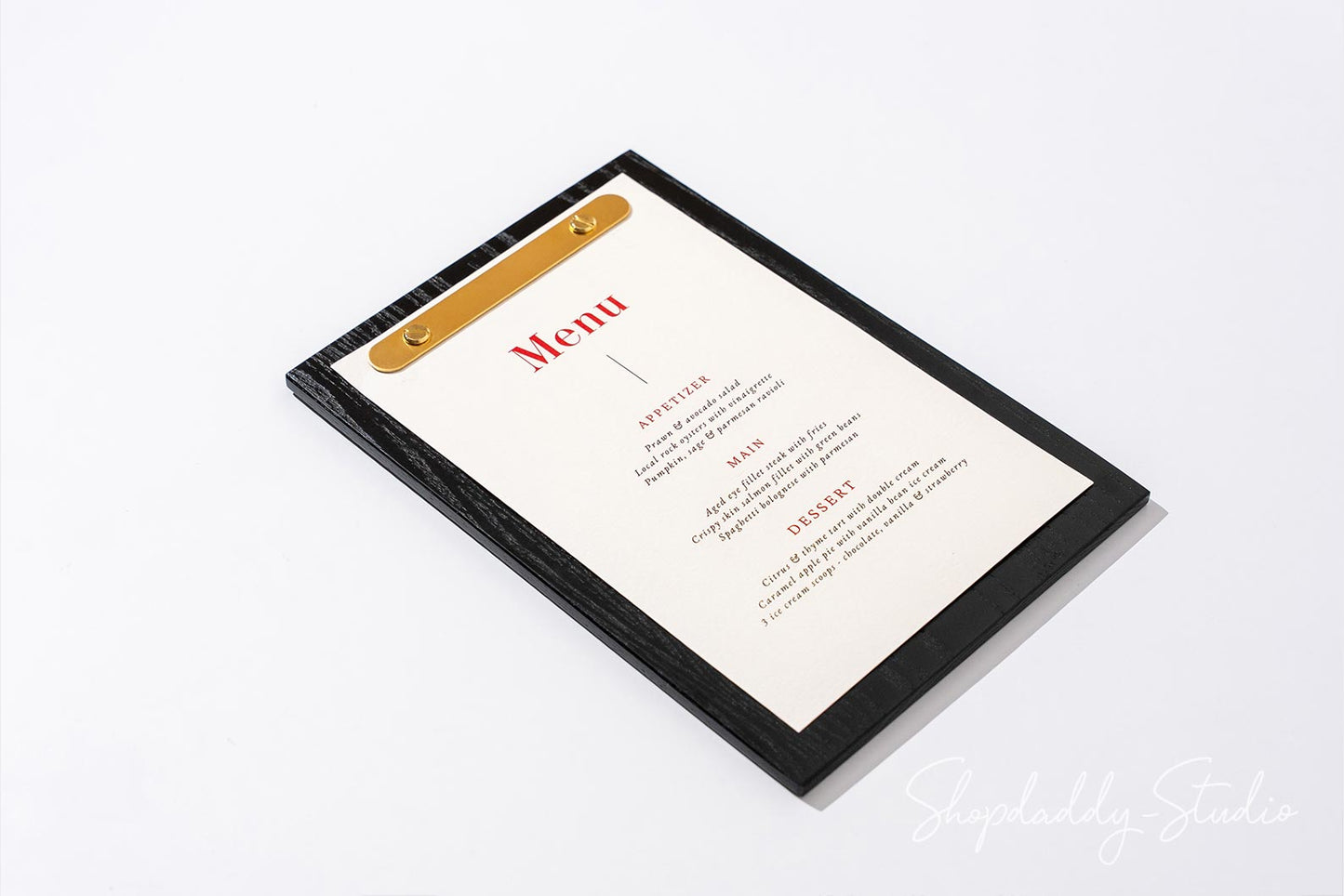 A black-framed clipboard menu holder with a gold metal clip and an off-white paper insert displaying a restaurant menu, photographed on a clean white background.