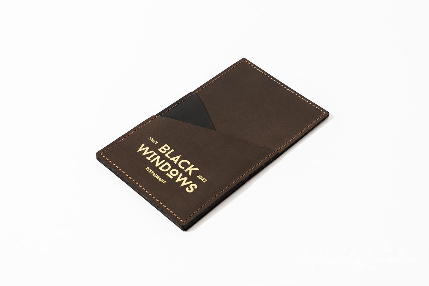 A dark brown leather card holder wallet with gold foil branding that reads 'BLACK WINDOWS' and 'MUNICH GERMANY', shown on a clean white background.