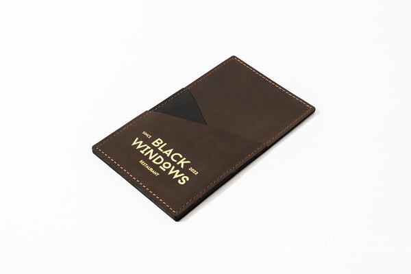 A dark brown leather card holder wallet with gold foil branding that reads 'BLACK WINDOWS' and 'MUNICH GERMANY', shown on a clean white background.