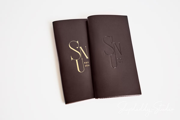 Two dark brown leather-bound notebooks with gold foil 'SNU EST 2025' monogram covers, displayed open on a clean white background.