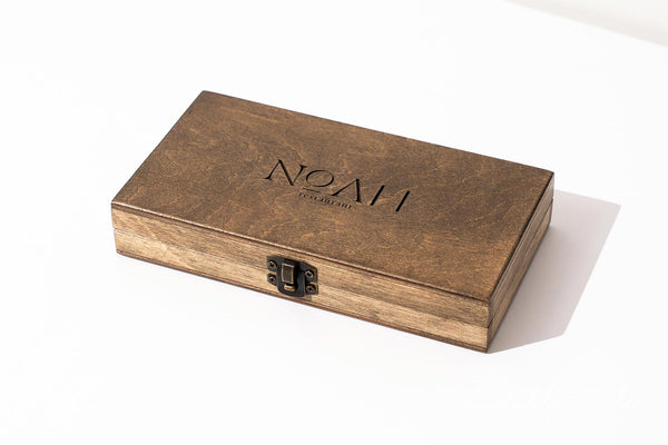 A rectangular wooden presentation box with a dark brown finish and a black metal clasp, featuring the brand name 'NOAH' embossed on the lid, set against a clean white background.