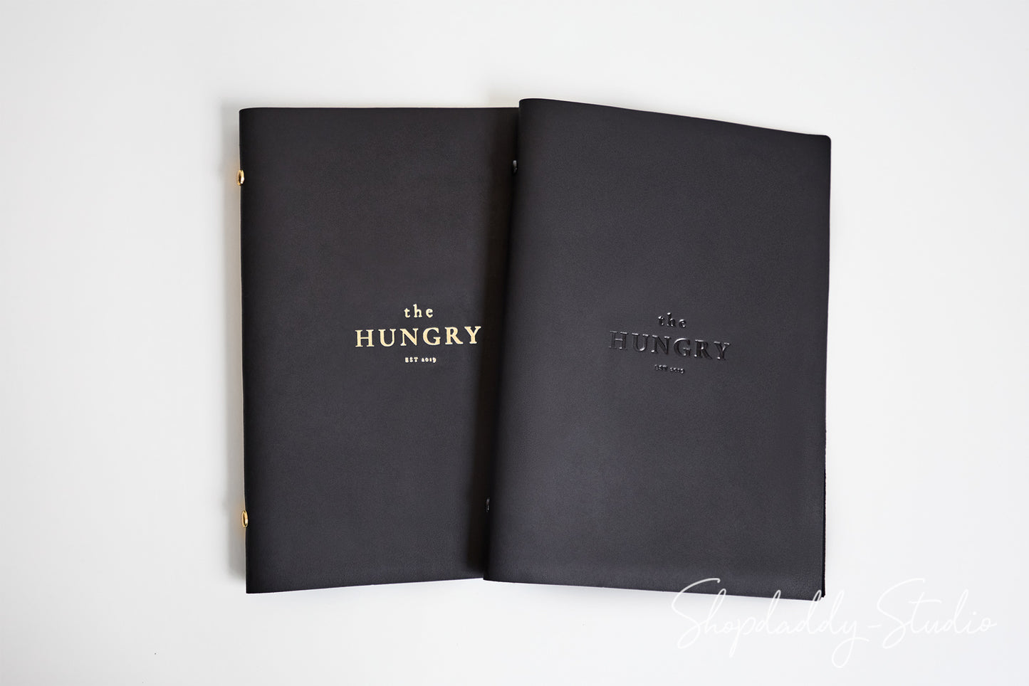 Two black hardcover books or portfolios titled 'the HUNGRY' with gold lettering, displayed side by side on a plain white background.