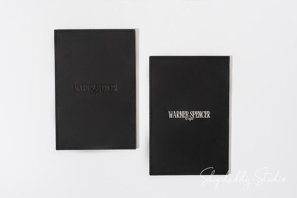 Two black leather-bound notebooks with 'Warner Spencer' embossed on the cover, displayed side-by-side on a clean white background.