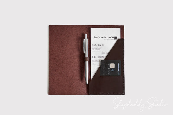 A dark brown leather organizer pouch shown open on a light gray background, containing a silver pen, a receipt, and a black card. A Shopdaddy Studio watermark is visible in the bottom right corner.