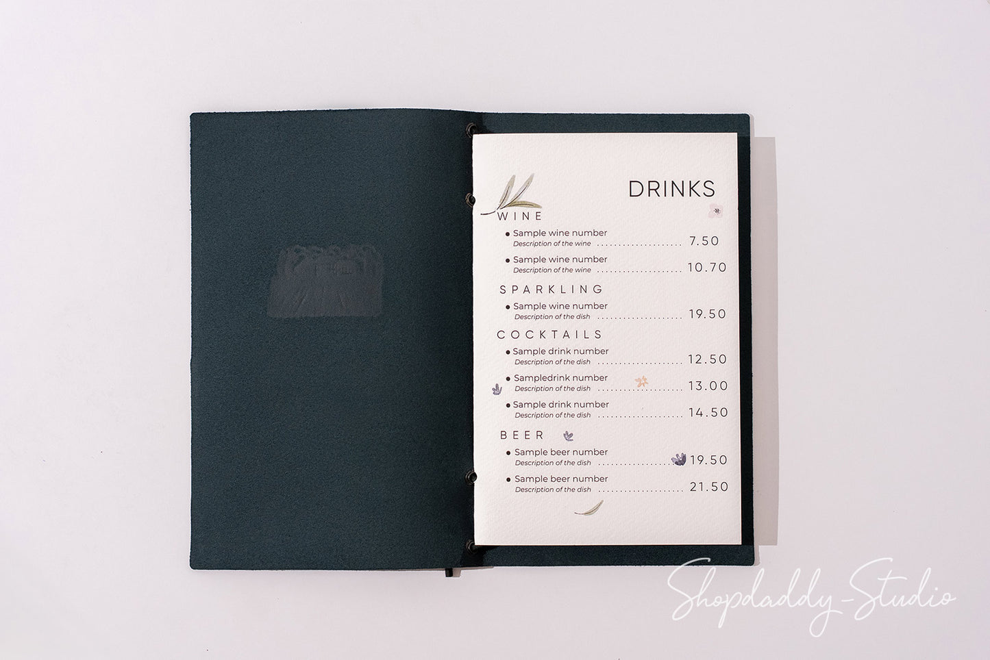 A dark teal or black menu book with an open page showing a printed drinks list, photographed from above on a plain white background.