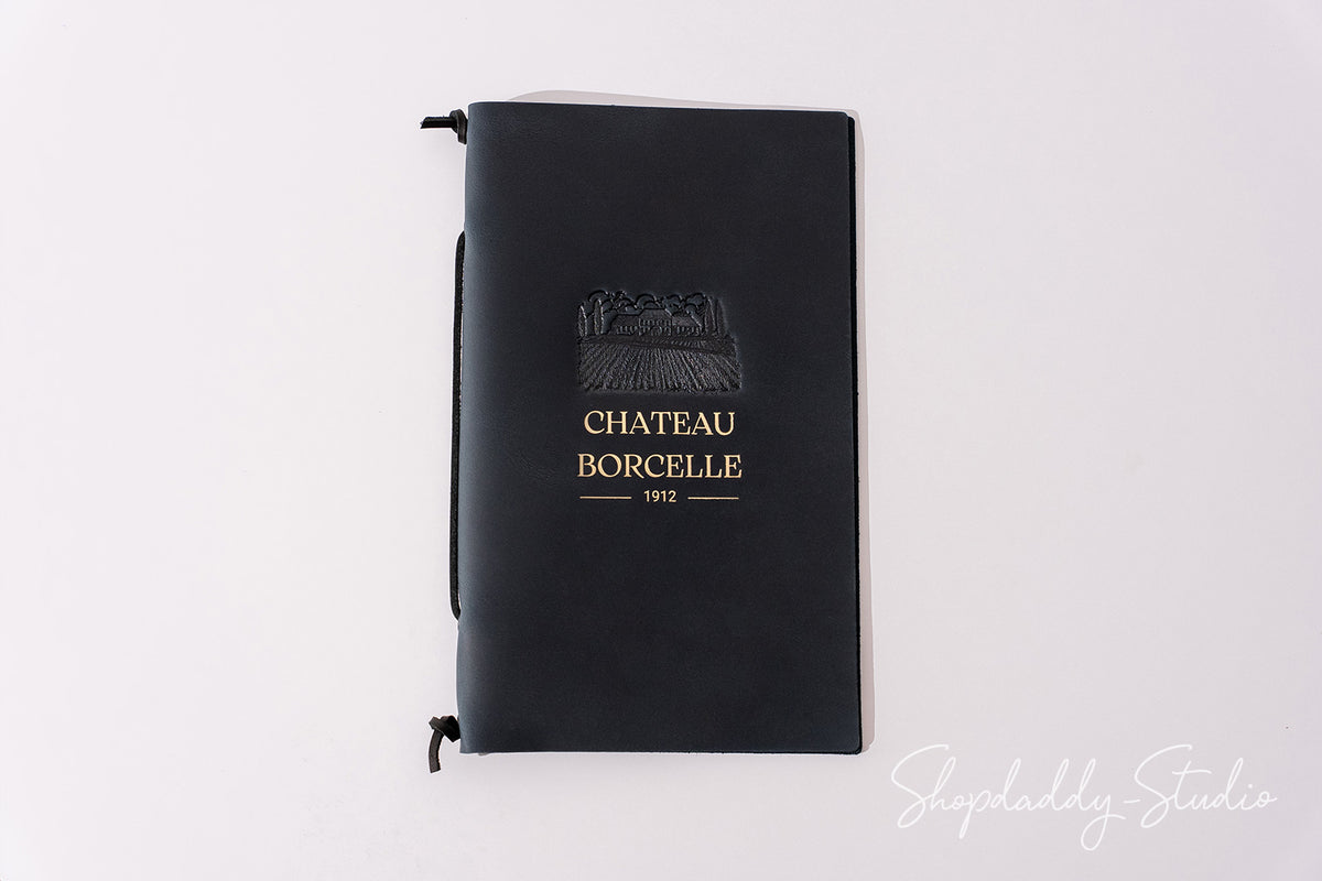 A black hardcover notebook with a gold embossed logo and text reading 'CHATEAU BORCELLE 1972' on the front cover, photographed against a plain white background.