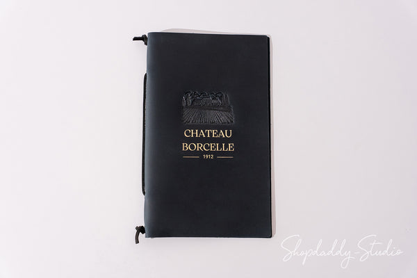 A black hardcover notebook with a gold embossed logo and text reading 'CHATEAU BORCELLE 1972' on the front cover, photographed against a plain white background.