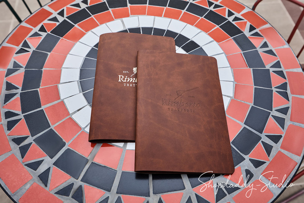 Two brown leather-bound notebooks or booklets with white printed text, placed on a circular mosaic table.