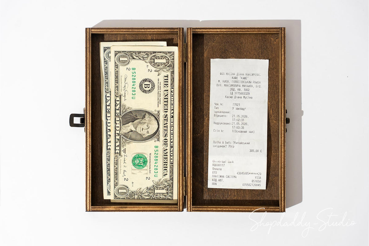 An open vintage wooden box with a black metal clasp, containing a stack of one hundred dollar bills and a handwritten receipt, photographed on a white background.