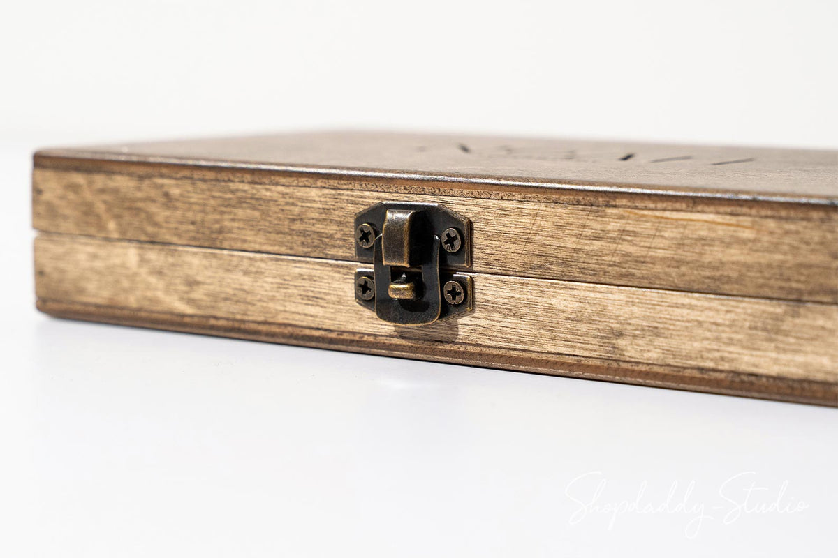 A close-up of a wooden jewelry box with a dark metal latch closure, showing the natural wood grain and texture on a white background.